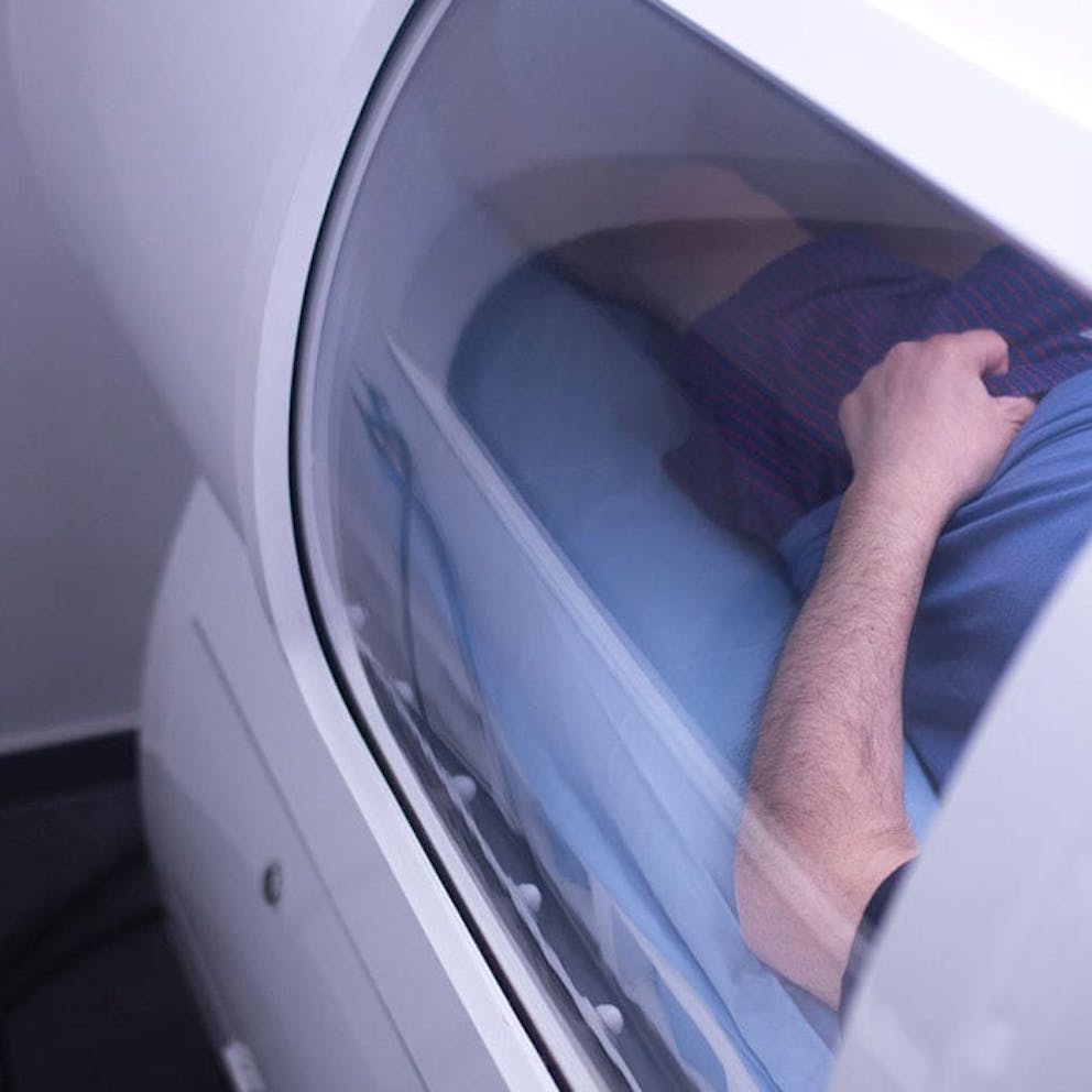 Man in hyperbaric oxygen therapy chamber looking in window to man’s arm and torso.