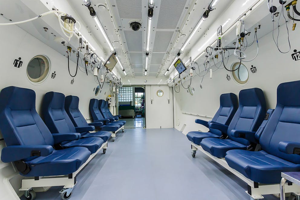 Large hyperbaric oxygen therapy room chamber with many chairs and medical equipment.