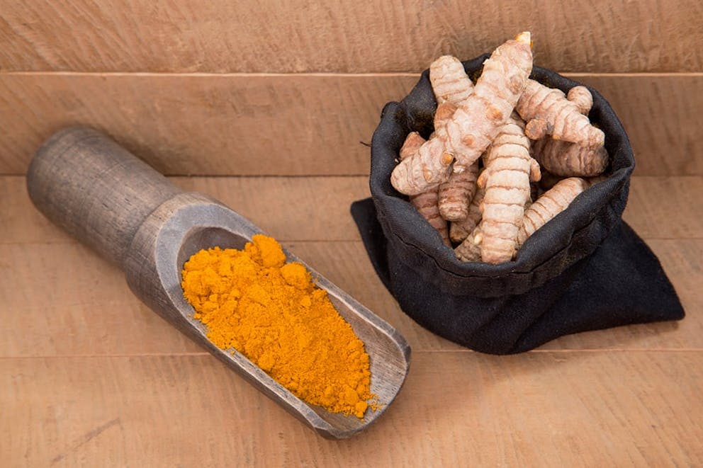 Turmeric root in cloth bag next to wooden scoop full of powder turmeric spice.