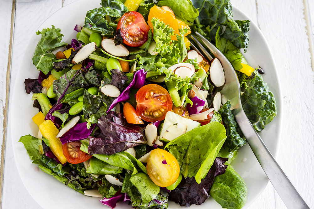 Healthy green salad with mixed greens and vegetables in a white bowl with a fork.