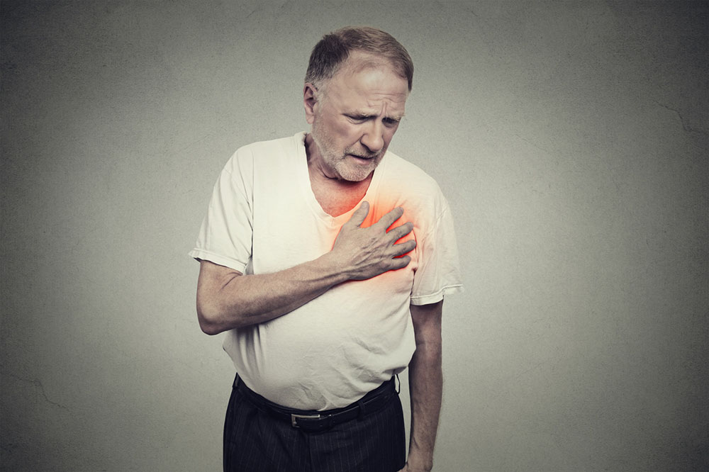 An elderly man suffering from chest pain clutching his chest, having a heart attack on a grey background.