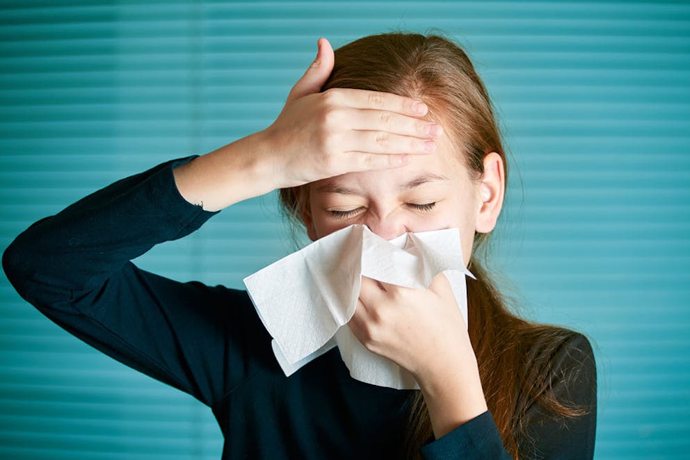Girl with allergies sneezing, holding her forehead, and blowing nose into tissue – nasal congestion.