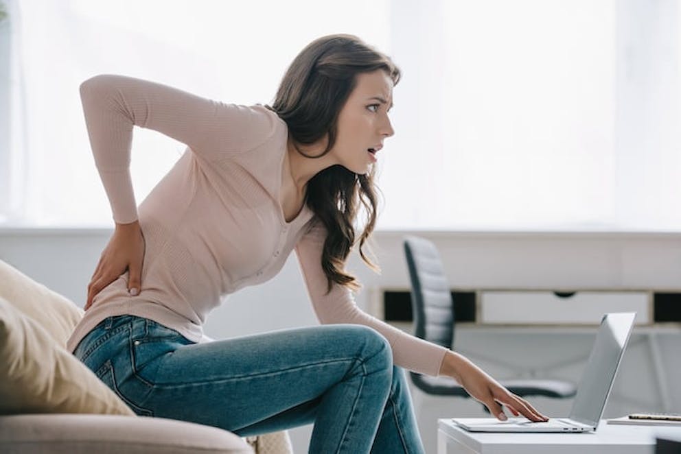 Woman hunched over with laptop experiencing back pain | Poor Posture Exercises