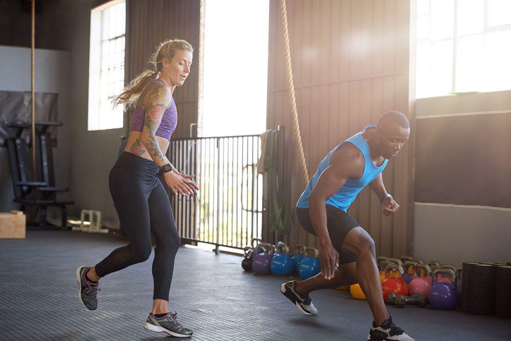 A woman and a man sprinting in workout clothes do high-intensity exercise interval training in a gym.