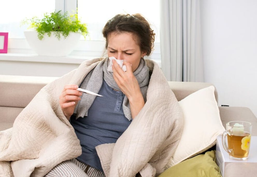 A woman with an infection sitting on a couch blowing her nose and checking her temperature | <u>The Effects of Autophagy on Infection</u>