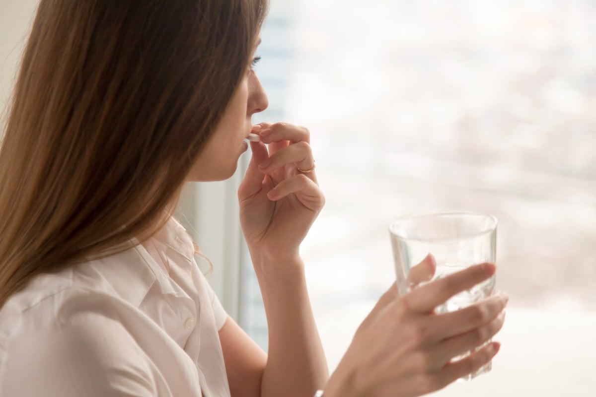 Young woman takes white round pill with glass of water in hand | The Heartburn Medication Myth
