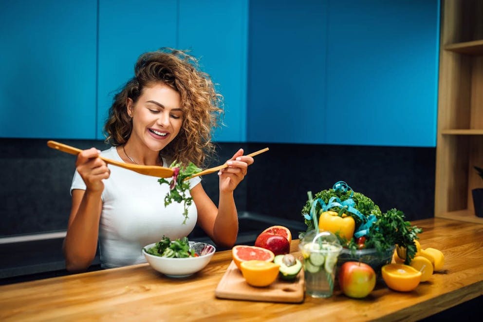 Young and happy woman eating healthy salad sitting on the table | Keto For Women: How Does Keto Affect Your Hormones | ketogenic diet women