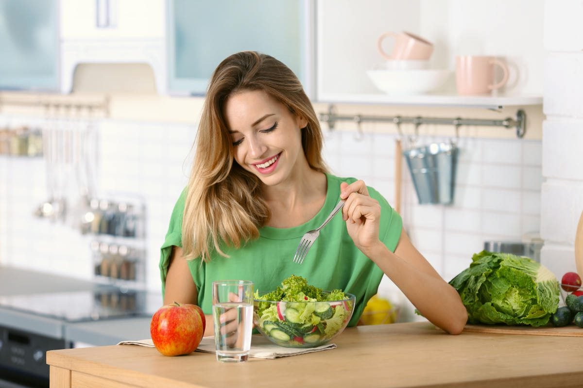 Woman eating vegetable salad at table in kitchen | How Can Trace Minerals Make Your Hair, Skin And Nails Healthier? | best hair skin and nails vitamins