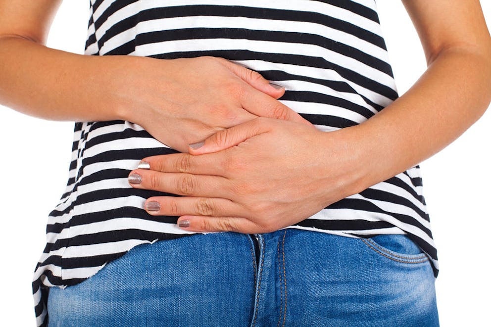 Woman in a striped shirt holding her hands to her stomach with bloating and digestive problems.