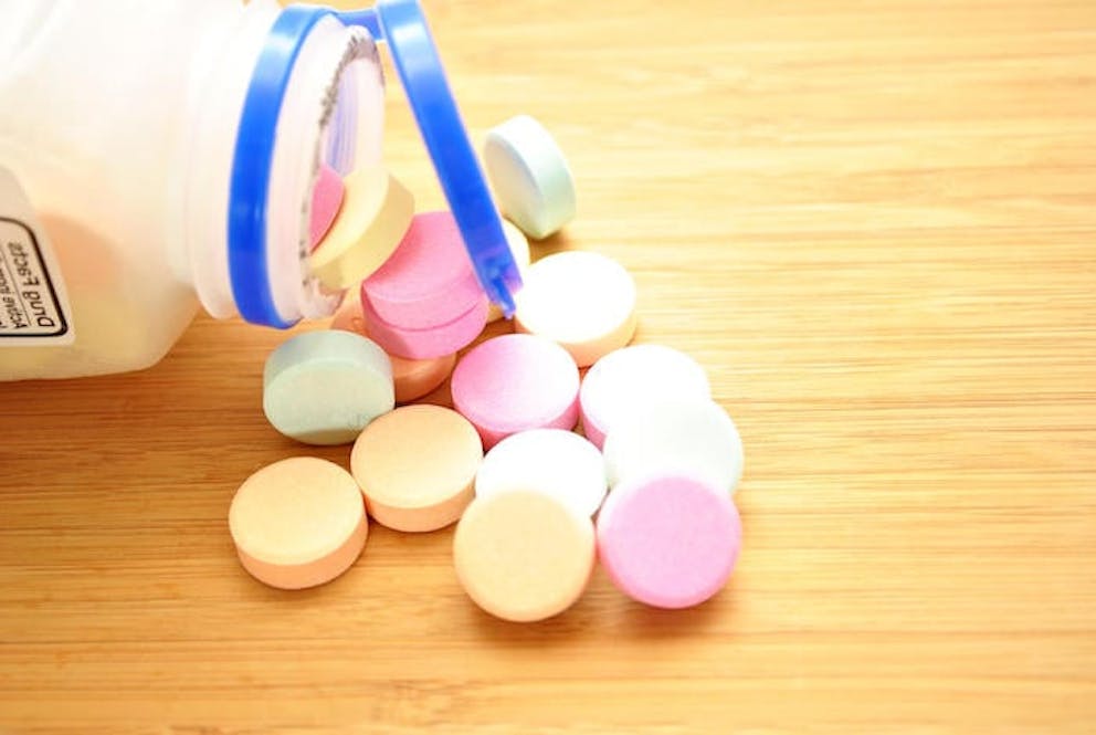A close-up of a bottle of colorful antacids spilled out on a wooden table