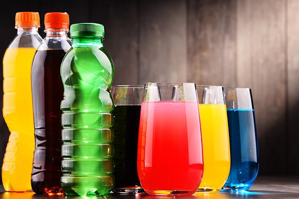 a picture of a variety of colored sodas in bottles and glasses