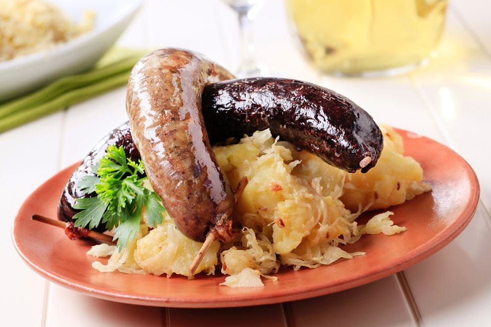 Two pork sausages over sauerkraut on a brown plate on white dinner table.