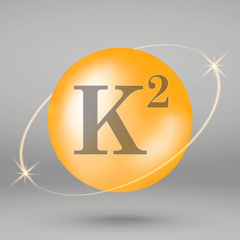Gold icon of vitamin K2, circle with letters surrounded by gold flash design.