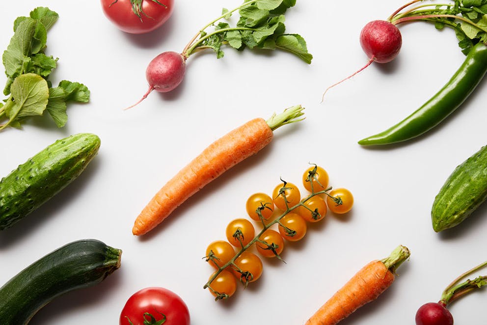 Assorted healthy vegetables on white background, carrots, tomatoes, radishes, cucumber.