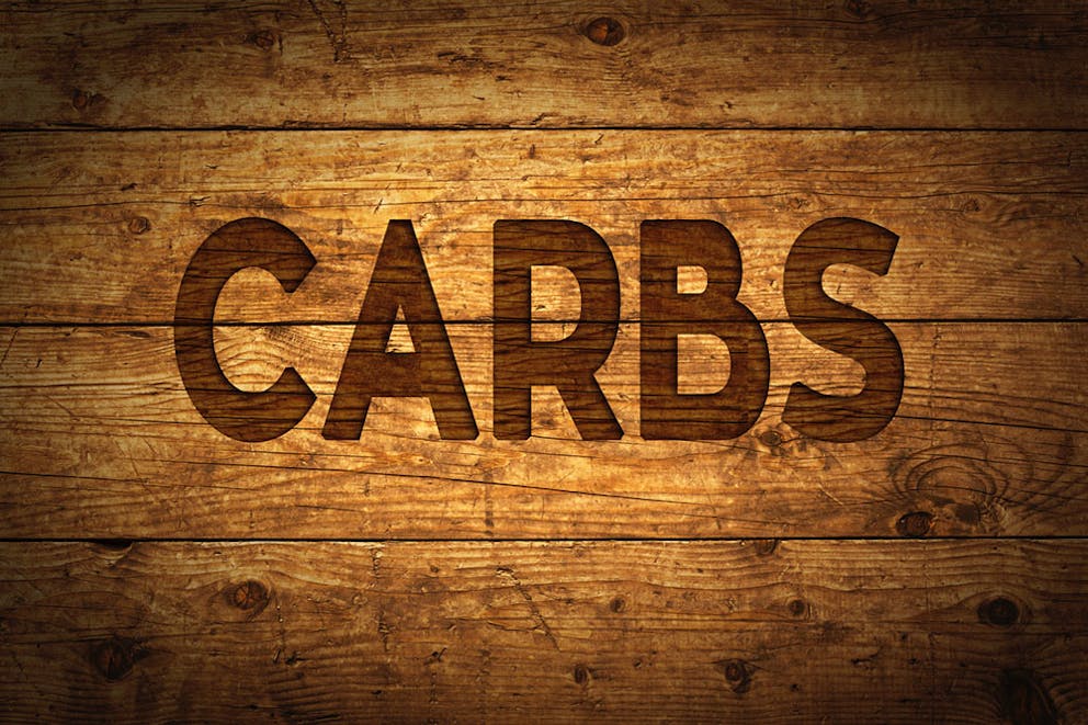 Carbs text in all caps written on wooden background, carbohydrates.