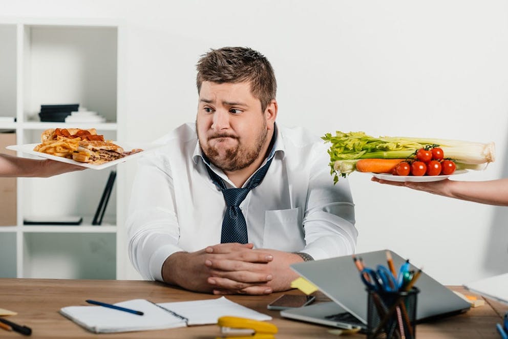 Overweight businessman choosing between healthy low-carb vegetables and unhealthy French fries.