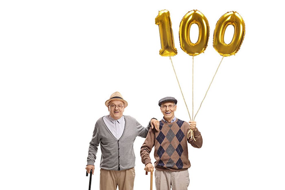 Two elderly men with canes smiling and holding balloons celebrating 100 years old.