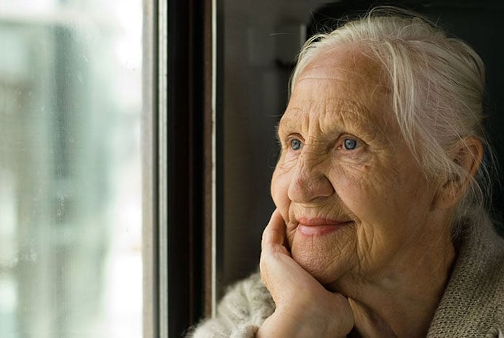Elderly woman with gray hair and wrinkles smiling and looking out a window.