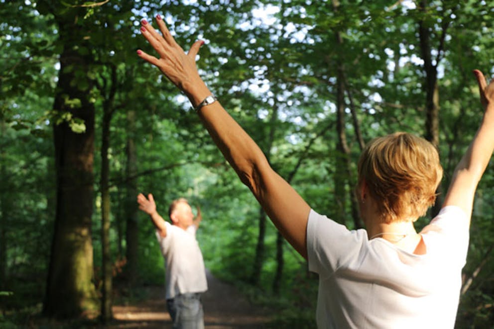 Man and woman in forest with hands in air forest bathing, breathe fresh air, health benefits nature.