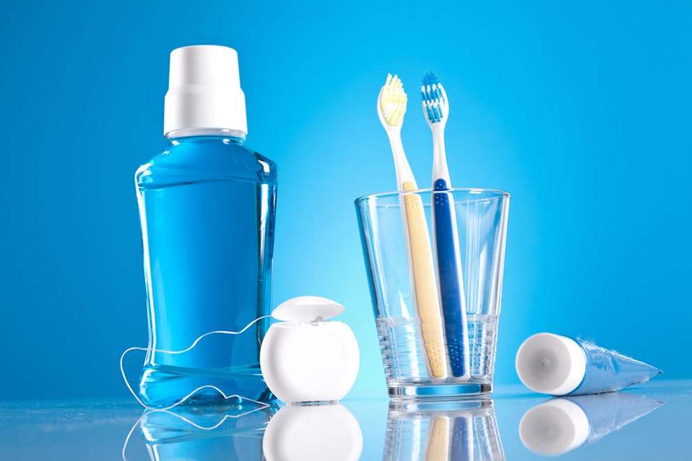 Bottle of mouthwash next to toothbrushes in glass and dental floss on blue background, dental care.