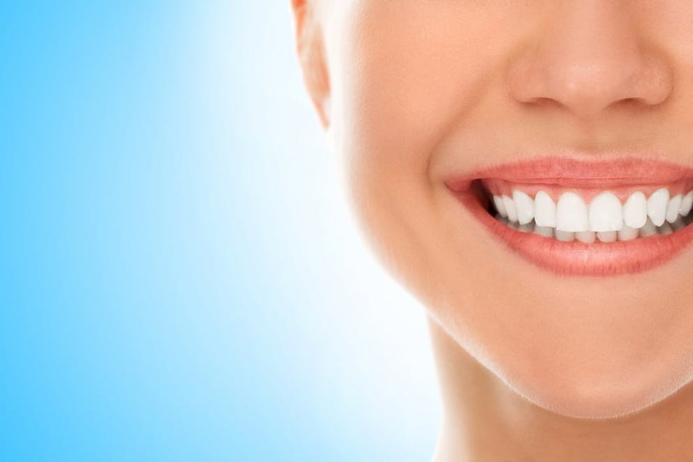 Woman smiling with white teeth on blue background, healthy teeth and gums, oral health.