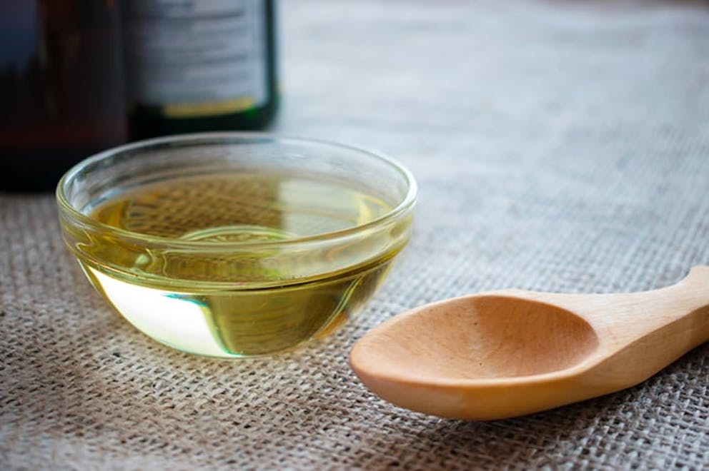 MCT oil supplement, MCT oil in glass bowl with wooden spoon, bottle in background on rustic cloth.