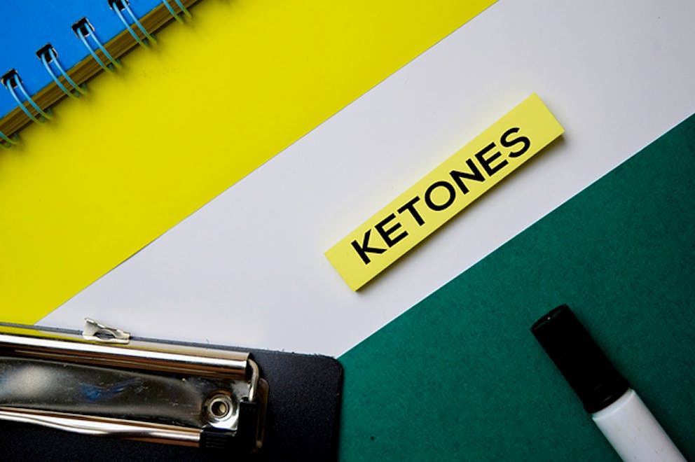 Ketones text on sticky note with office supplies and marker nearby. Keto diet, ketone fuel.