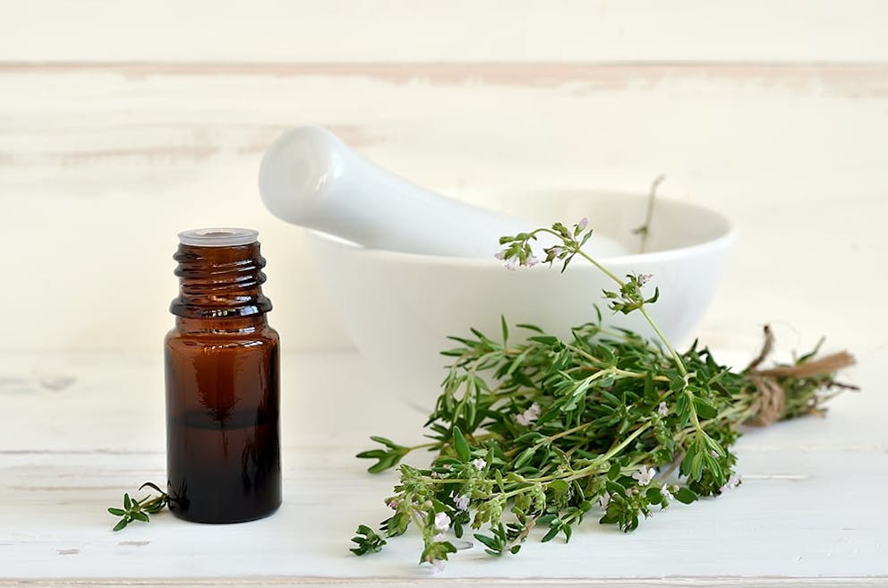 a photo of a bottle of thyme oil alongside sprigs of thyme in a bowl