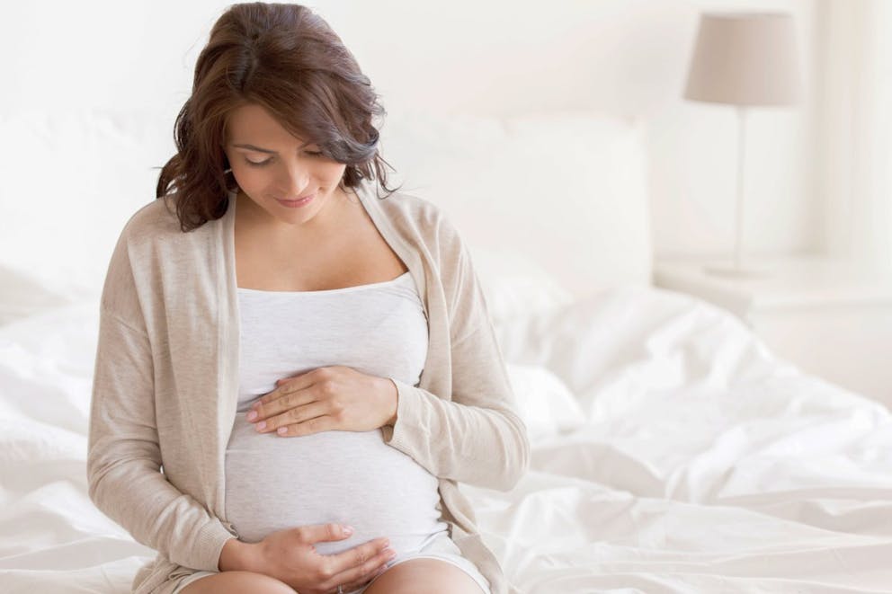 Happy pregnant woman sitting on bed and touching her belly | Use Vitamin D To Keep Viruses In Remission In Winter Months | vitamin d fights viruses