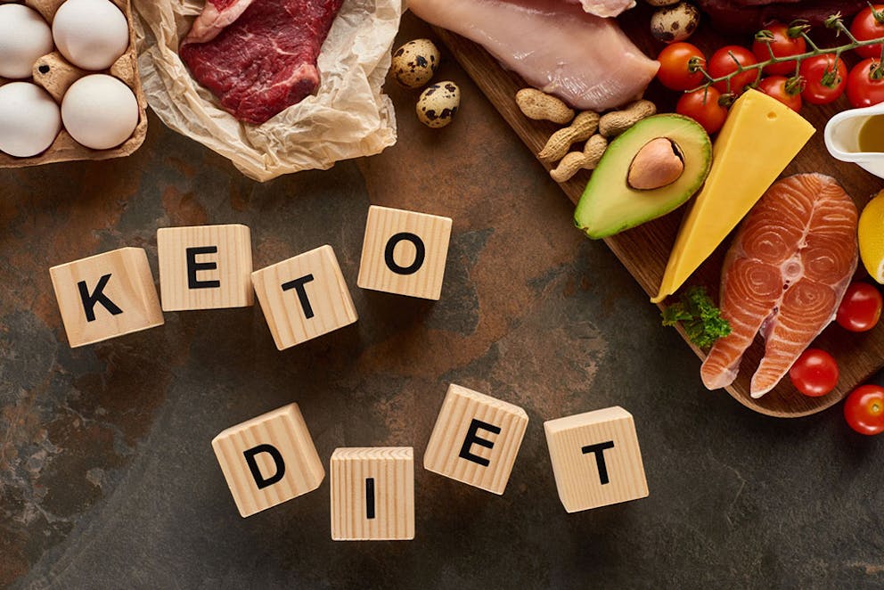 Wood blocks spelling keto diet on slate surface surrounded by ketogenic diet healthy foods.