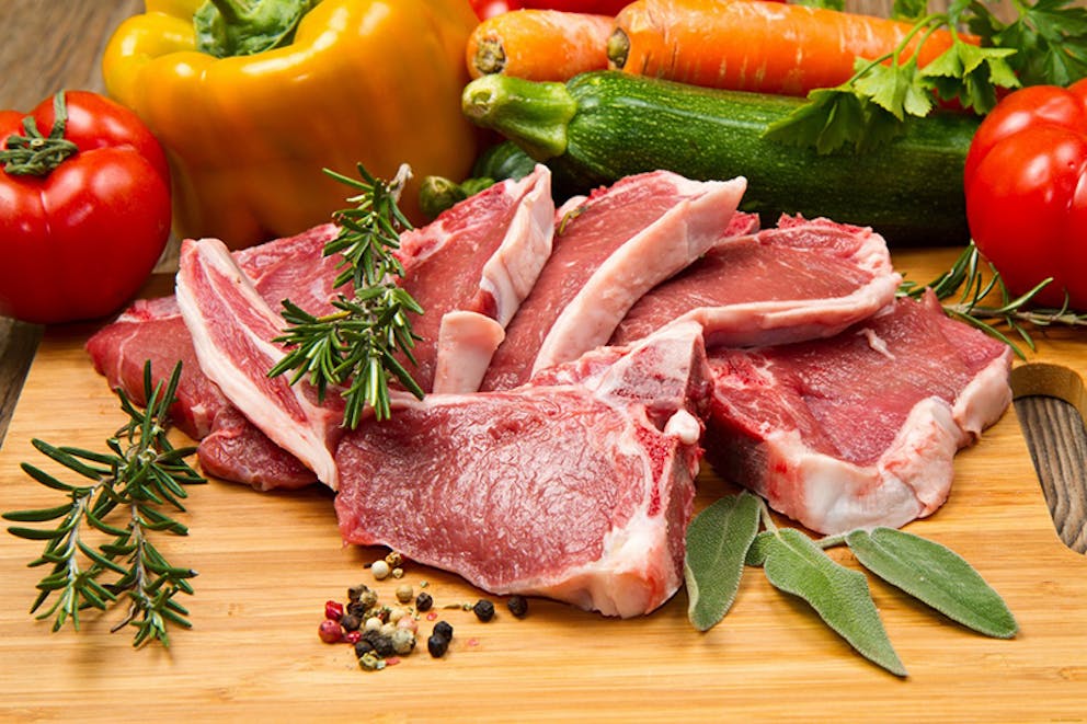 Close-up photo of meat and vegetables, steaks with peppers, tomatoes, zucchini, on cutting board.