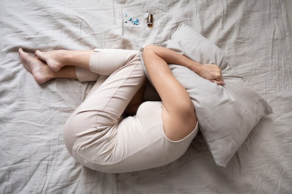 a stressed woman lying in bed covering her head