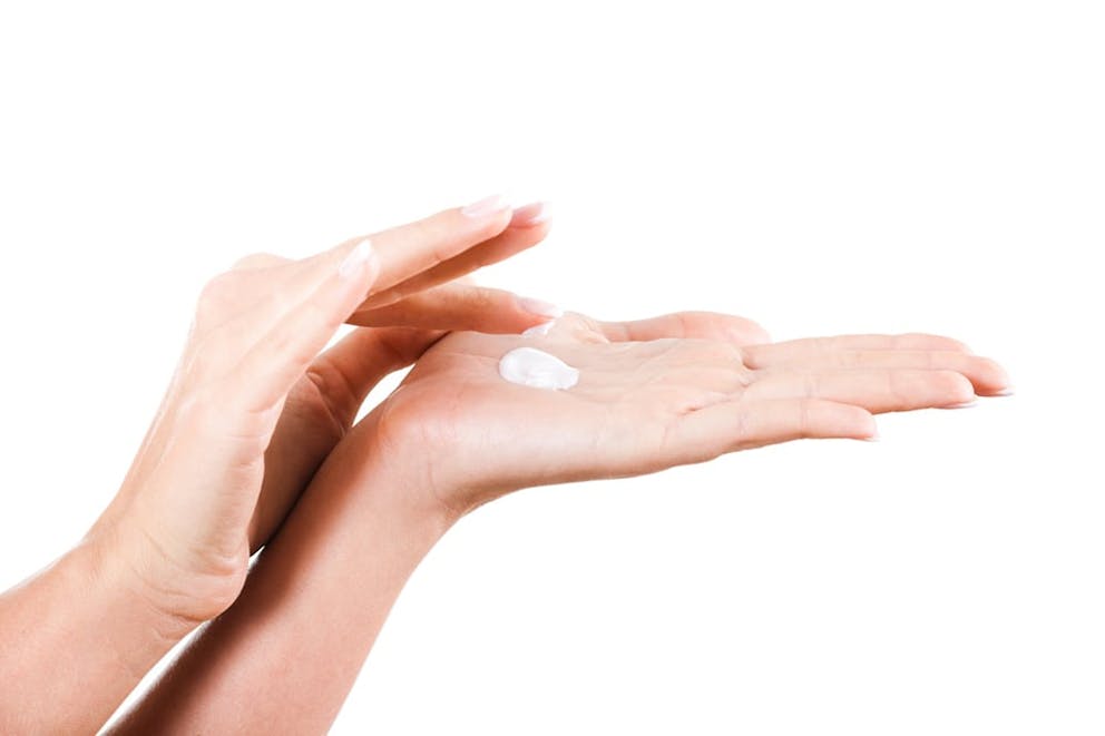 Woman’s hands on white background with topical cream in palm, using fingers to spread.