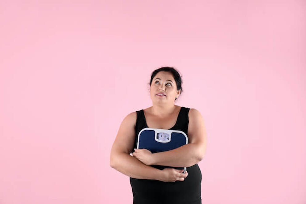 Obese woman holding a scale with a pink background | What is Your Body Type?