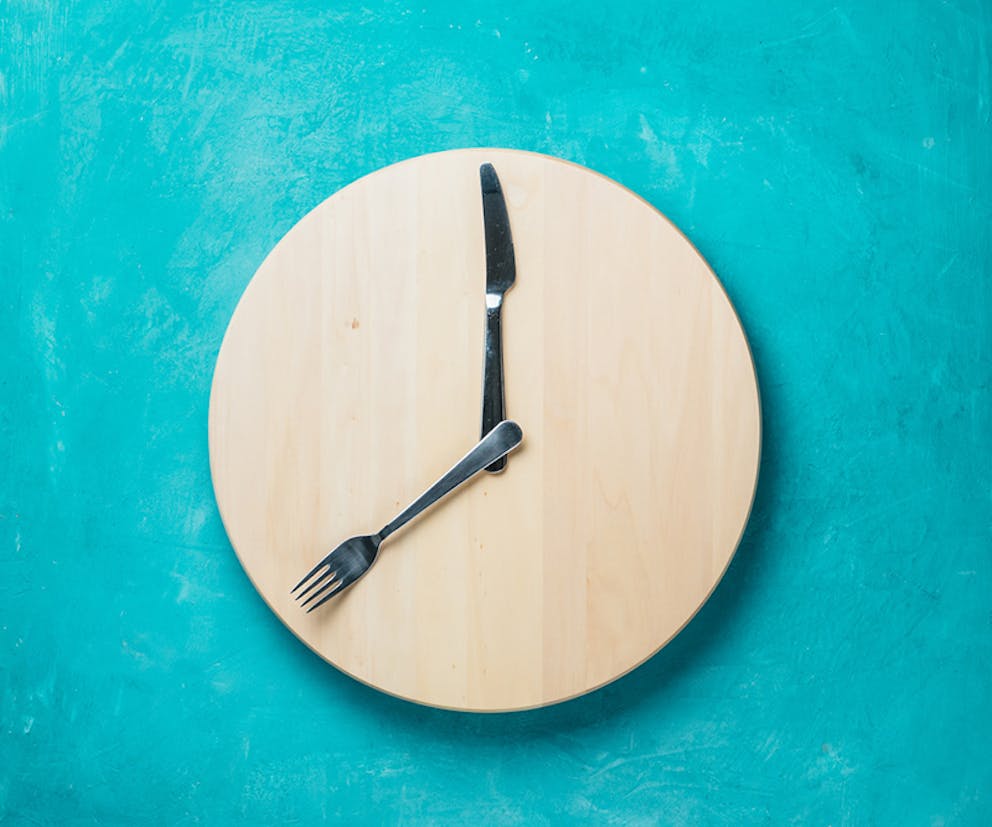 Fork and knife on wood circle making a clock out of silverware, intermittent fasting concept.
