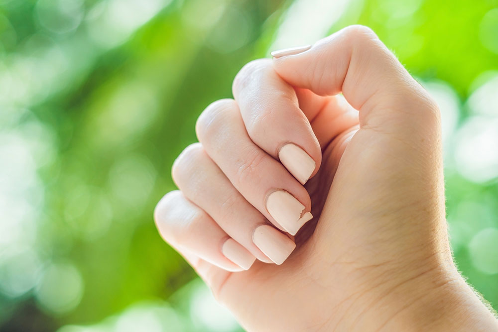 Broken nail on a woman’s hand with a manicure on a green background