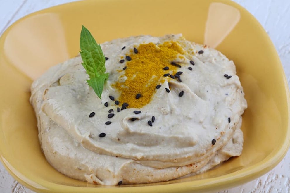 Close up of hummus in yellow bowl topped with sesame seeds and spices, tahini butter.