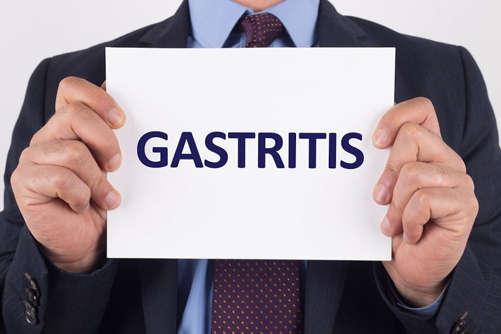 Businessman in suit holds white paper that says gastritis, stomach inflammation.