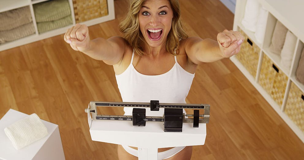 a happy woman standing on a scale and celebrating her weight loss