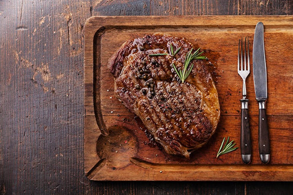 a photograph of a grilled steak on a plate next to a fork and knife