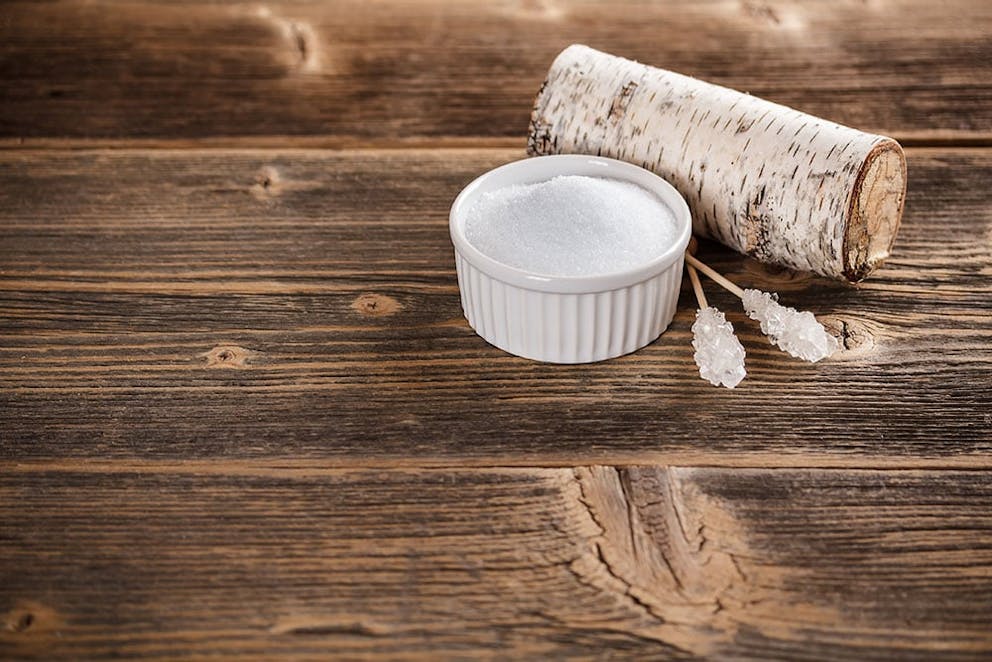 a bowl of xylitol with a birch branch with bark behind the bowl