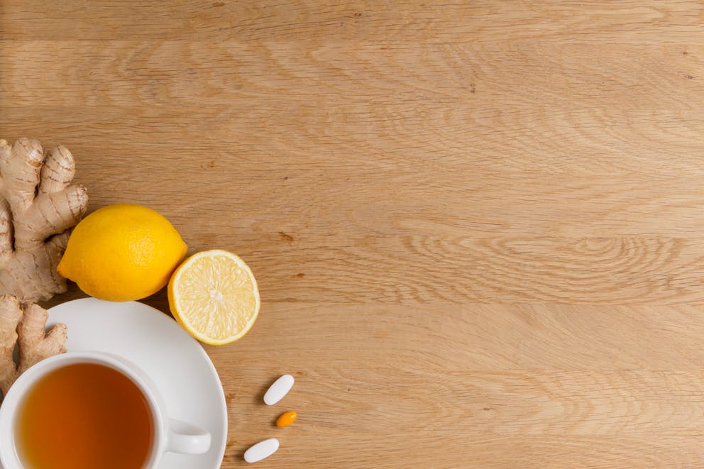 A cup of tea surrounded by lemon, ginger, and vitamin supplements on a wooden table.