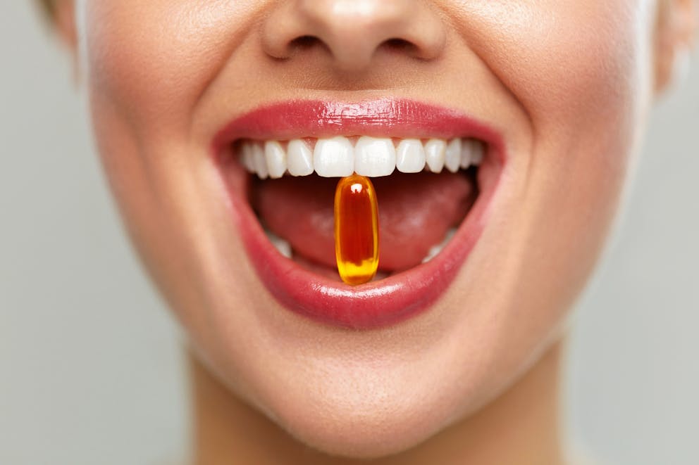 Woman with vitamin D capsule in between teeth