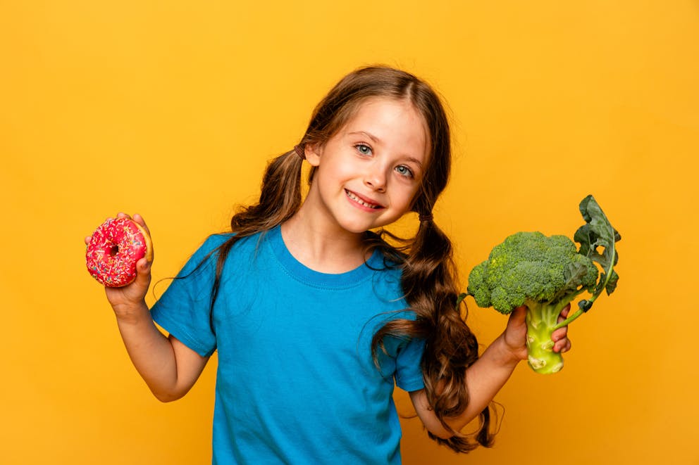 Girl holding doughnut and broccoli