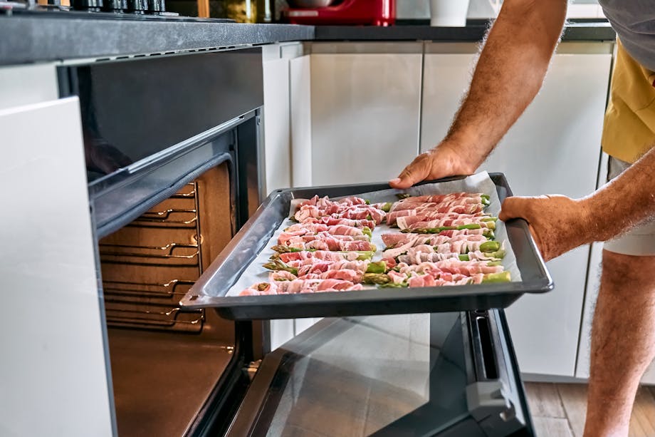 Placing asparagus wrapped in ham in the oven