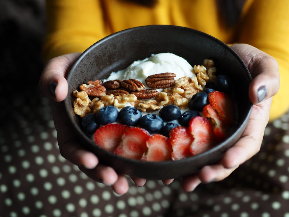 Plain Greek yogurt topped with pecan, walnut, blueberry, and strawberry in a dark brown ceramic bowl