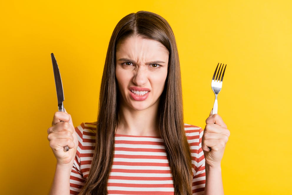 Frustrated hungry woman holding utensils