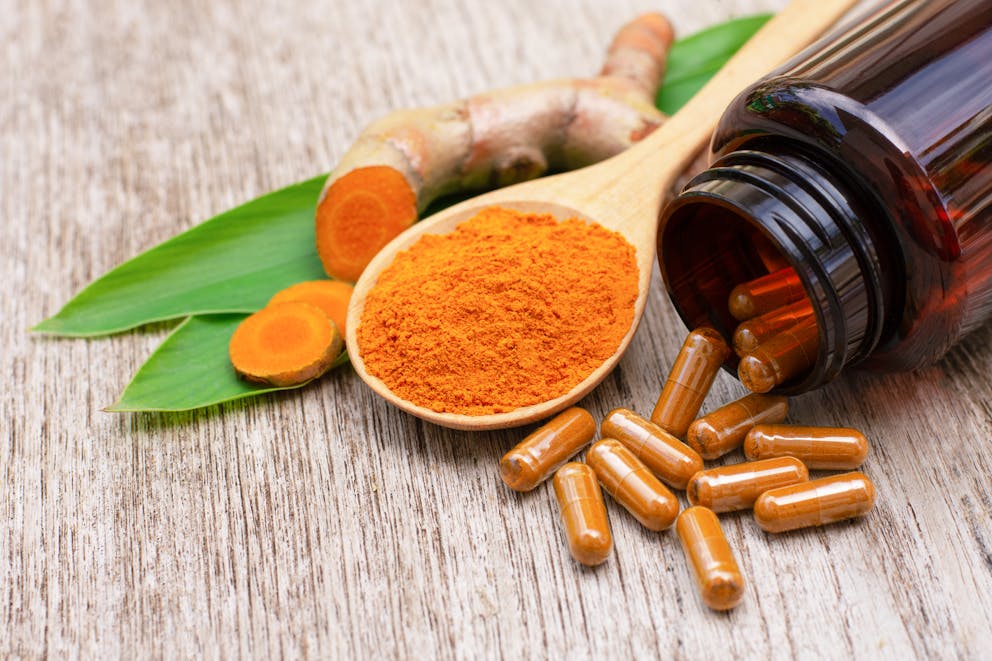 Turmeric powder capsules and turmeric root with green leaf